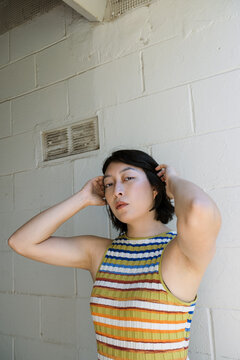 Non-binary person in striped dress against white cement wall