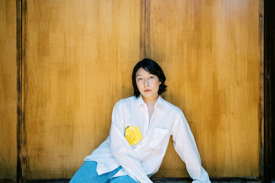 Non-binary person sitting in front of warm toned wood wall
