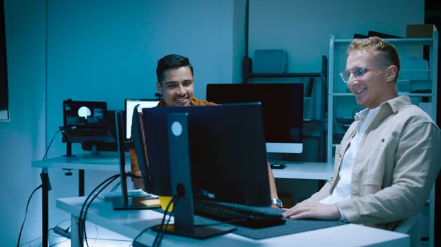 Two happy young male IT specialists giving high five celebrating successful computer software programming code and artificial intelligence data analysis development in office