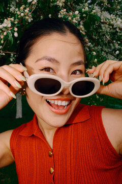 Smiling woman in sunglasses portrait with blooming trees