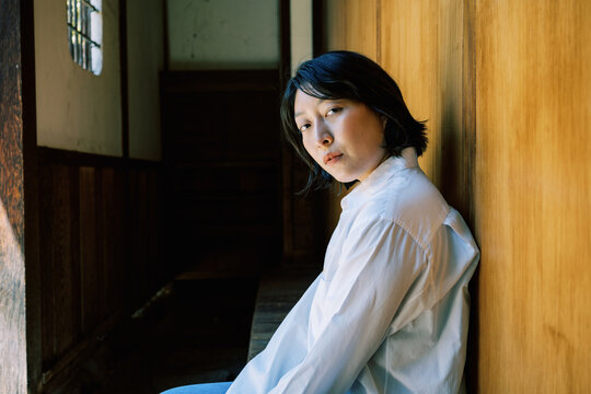 Non-binary person leaning against warm toned wood wall