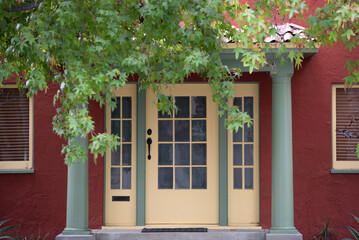 Naklejka premium Entrance with classic residential architecture details. Entrance with symmetrical facade and columns. Entrance framed by green leaves and porch. Entrance representing cozy suburban housing.