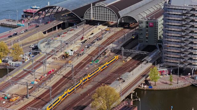 High angle inspection of Amsterdam Centraal railway station showing modern yellow train departing from busy hub and ongoing platform improvement works