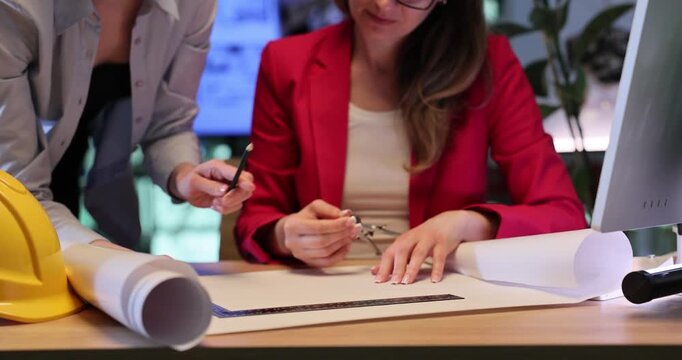Architectural designers use compass and ruler to draw building sketch on large sheet of drafting paper. Women create building sketch. Slow motion