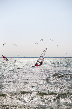 Windsurfer gliding fast through choppy sea waves with colorful kitesurfing sails during summer sports event. Chalupy, Hel Peninsula, a famous Polish travel destination packed with professional surf sc