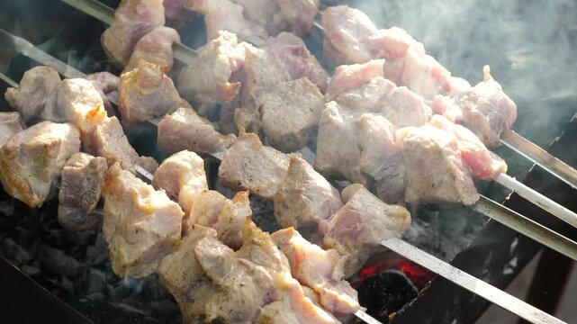 Juicy pork shish kebab on skewers appetizingly grilling over hot charcoals. The process of cooking marinated meat on a mangal with thick aromatic smoke during a picnic.