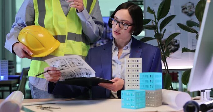 Businesswoman discusses important construction stages with builder. Focused woman reviews sophisticated building sketches. Slow motion