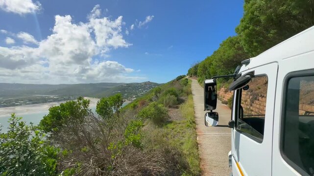 Tourist vehicle travels along a coastal road with views of the Knysna Lagoon and Featherbed Bay in South Africa.