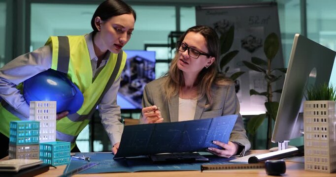 Experienced builder and professional architect discuss detailed building drawings. Women consider modern building plans together. Slow motion