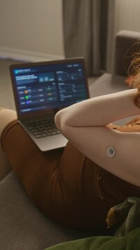 Vertical over shoulder shot of pregnant Caucasian young adult woman with glucose monitor on arm typing on laptop. Perfect for promoting gestational diabetes tech and prenatal health apps