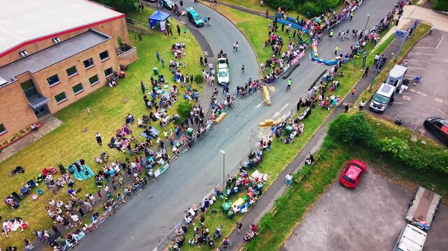 Editorial aerial footage of a soapbox derby community event in Andover, Hampshire, England, showing spectators lining a closed road, industrial buildings, race barriers, hay bales