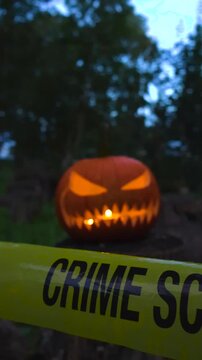 Creepy glowing Jack o' lantern with a sinister face sitting in a dark forest at dusk, with yellow police caution tape marking a crime scene in the foreground for a spooky concept