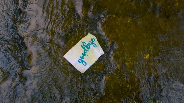 Handwritten goodbye note on a piece of paper floating down a shallow river, representing the end of a relationship, sadness, letting go of the past, and moving on to a new beginning