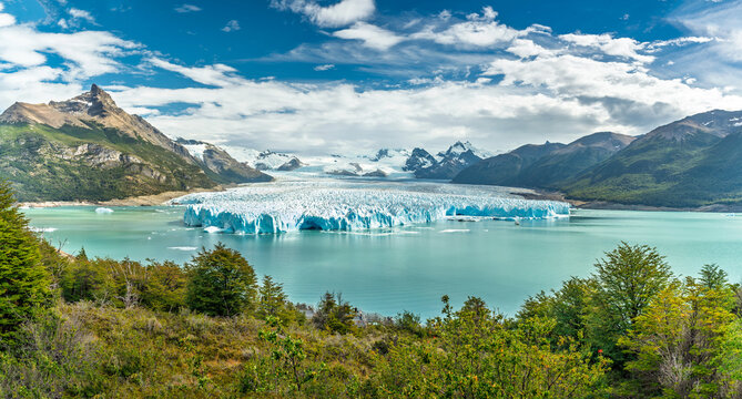Panoramic view of Perito Moreno Glacier in Los Glaciares National Park, Patagonia, Argentina, massive blue ice wall meeting turquoise water of Lake Argentino under blue sky