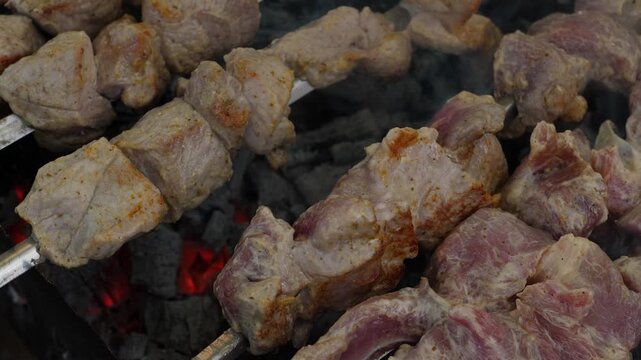 Appetizing pork shish kebab close-up roasting on skewers over a mangal grill. The process of cooking juicy marinated meat over hot wood charcoals with smoke