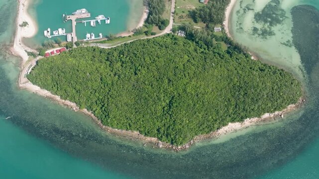 Top view of lush greenery covering a small island, turquoise waters with visible reefs, and a nearby pier with boats. Lipa Noi. Ko Samui, Thailand.