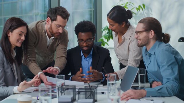 African American businessman boss with multiethnic business team discussing papers stats at office meeting. Five diversity managers talking considering project results documents at table teamwork