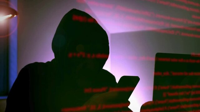 Anonymous hacker in a hoodie using a smartphone in a dark room with code
