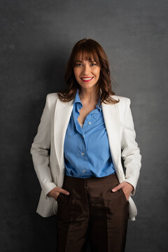 Confident businesswoman in white blazer smiling against dark studio background