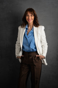 Confident businesswoman in white blazer smiling against dark studio background
