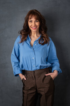 Smiling confident woman in blue shirt standing against dark studio background