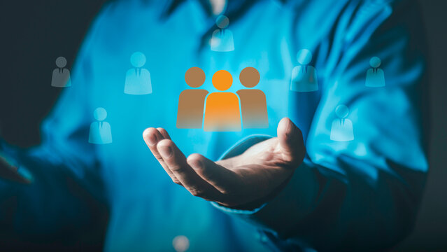 Concept of human resources management, leadership, recruitment vetting, talent selection and team building for business success. Hand holding orange people icon among blue silhouettes.