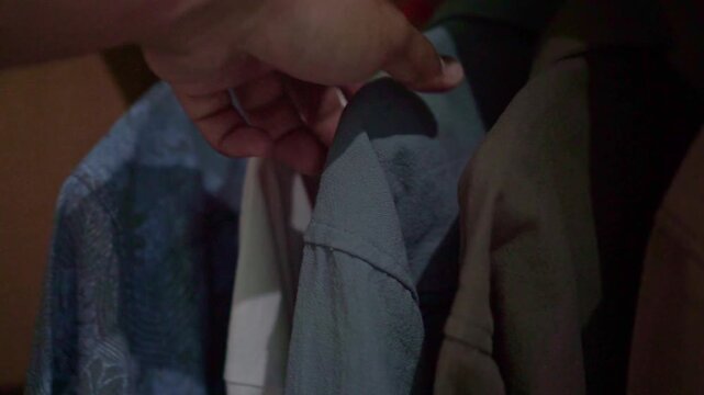 Hand placing apparel on a hanger inside a wardrobe, representing storage efficiency, clothing management, home organization, and daily chores.
