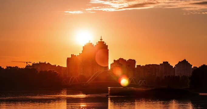 Beautiful sunset over Obolon Embankment in Kyiv, Ukraine, featuring the iconic Wave Bridge, calm reflections on the water, and a glowing city skyline in warm evening light.