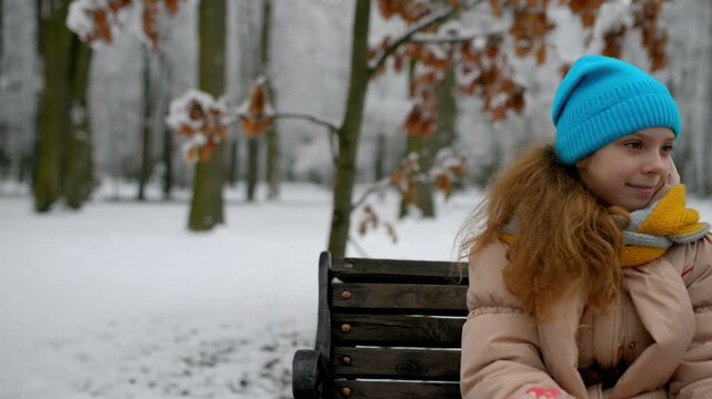 Little girl sits on bench in winter park