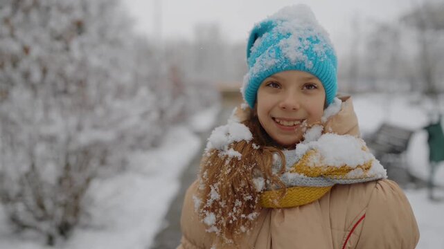 little beautiful girl in a beige jacket is walking along a path in a snowy park
