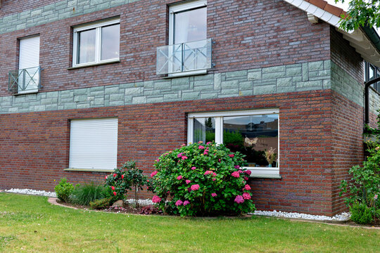 Exterior view of a contemporary residential house built with red clinker bricks and stone accents, featuring a large pink hydrangea shrub in the front yard.