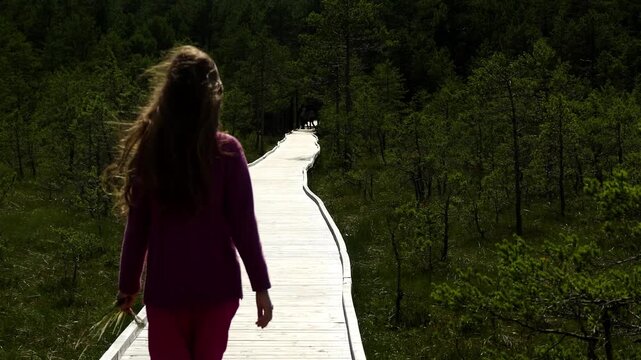 Little girl with long hair goes on a wooden walkway in the national natural nature reserve.