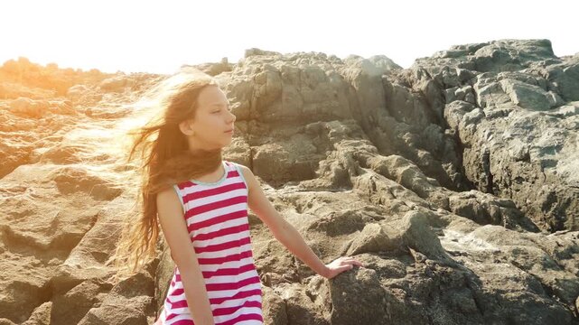 Little girl sitting on rocky shore of sea