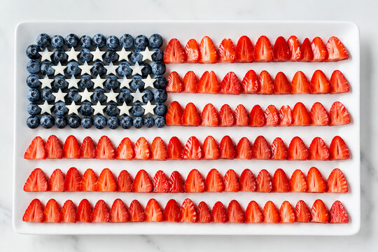 American flag shape made of fresh blueberries and sliced strawberries on white rectangular serving.