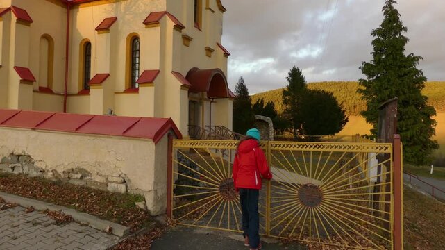 Little beautiful girl in red jacket walks near Church St. Stefan Uhorskeho, Janovce-Cencice, Slovakia.
