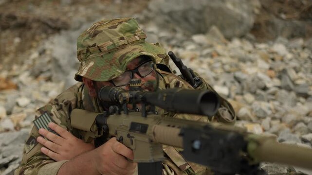 A special forces soldier aims a sniper rifle with intense focus, conducting surveillance during a tactical mission in a rugged, rocky terrain.