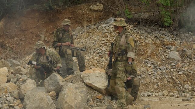 A tactical military squad takes a break during a reconnaissance mission, strategizing while resting with their rifles in a rugged and rocky environment.
