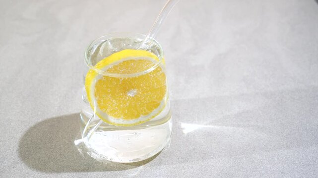 Lemon water in a glass on a gray concrete table with sun glare