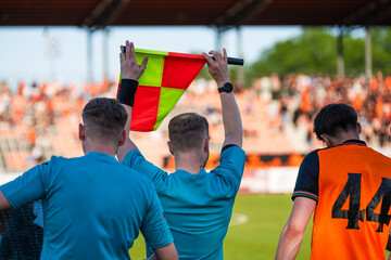 Assistant referee holding a flag during a soccer match while officials and substitute players stand near the touchline © Dziurek