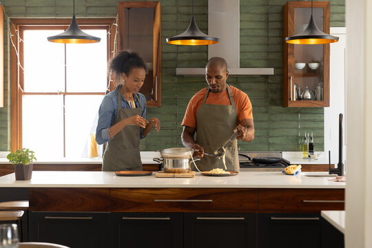 Couple wearing aprons cooking at home kitchen island, stirring frying pan and seasoning pot