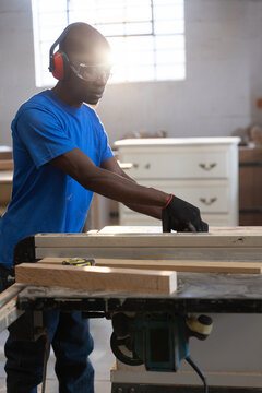 Table saw slicing wood planks in carpentry workshop, sunlight streaming through large grid window