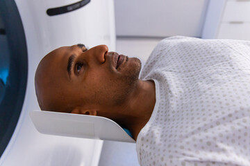 Fototapeta premium African American man lying with molded head support inside scanner bore during head scan at clinic