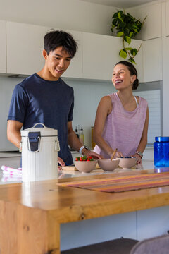 Couple standing at kitchen island preparing three fruit bowls on wooden cutting board, smiling
