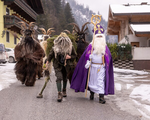 Obraz premium Festive event in winter with people in costumes walking on a snowy road near houses in the mountains, Dorfgastein, Austria