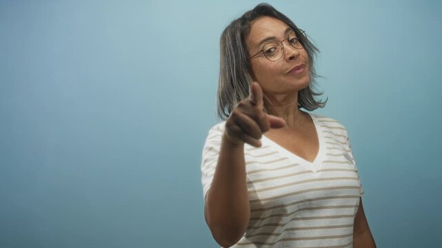 Woman points finger at camera wearing glasses and striped shirt in studio with slight head tilt and direct gaze; assertive confidence.