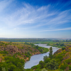 Fototapeta premium view from green rocky hills to the river in the canyon under a blue cloudy sky