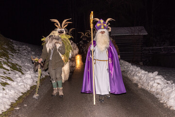 Obraz premium Festive parade features figures in costumes walking on snowy road at night in winter festival celebration, Austria