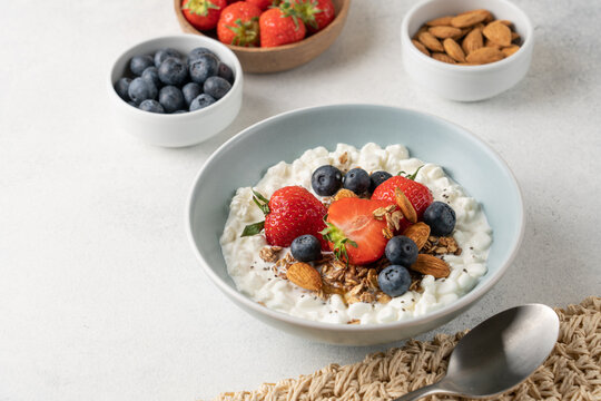Fresh high protein cottage cheese berry bowl with blueberries, strawberries, chia seeds, granola and almonds served on light background with copy space