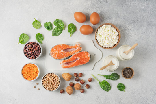 High protein food set with fresh salmon, eggs, cottage cheese, yogurt, lentils, chickpeas, beans and nuts arranged on white background with copy space