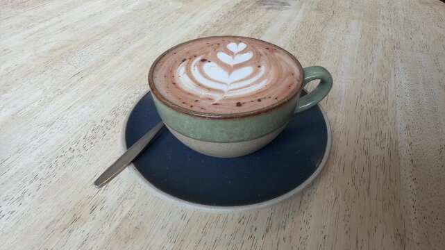 Delicious hot chocolate in cute ceramic cup with beautiful floral ornament on top of thick milk foam, perfect for cozy morning breakfast or relaxing coffee break inside a warm aesthetic cafe